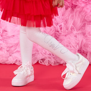 White sneakers with bows worn with a red dress on a pink background