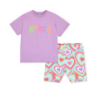 The Eloise set is the ultimate cycling short set of the season. It comes with a purple top featuring a multi coloured sequin logo across the front and matching heart print cycling shorts.