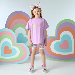 The Eloise set is the ultimate cycling short set of the season. It comes with a purple top featuring a multi coloured sequin logo across the front and matching heart print cycling shorts.