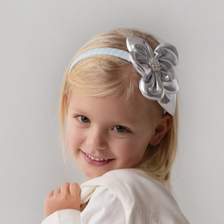 Young girl wearing a silver headband with a large flower on a plain background