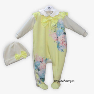 Lemon baby grow for girls by Petit Italia it has blue and pink flowers on the front with a scalloped collar and lemon satin bow with petit written in dimantes on the collar it is matched with a white hat with a lemon satin bow on the front.