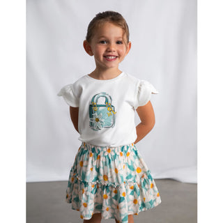 Young girl wearing a white shirt with a lock design and a floral skirt against a plain background